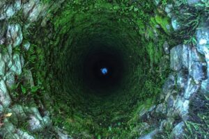 A deep old, stone, mossy well, seen from above